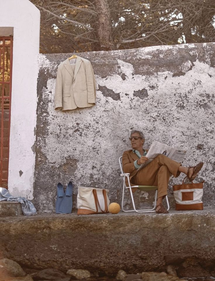 Man reading beside a weathered coastal wall with collected bags and swim fins
