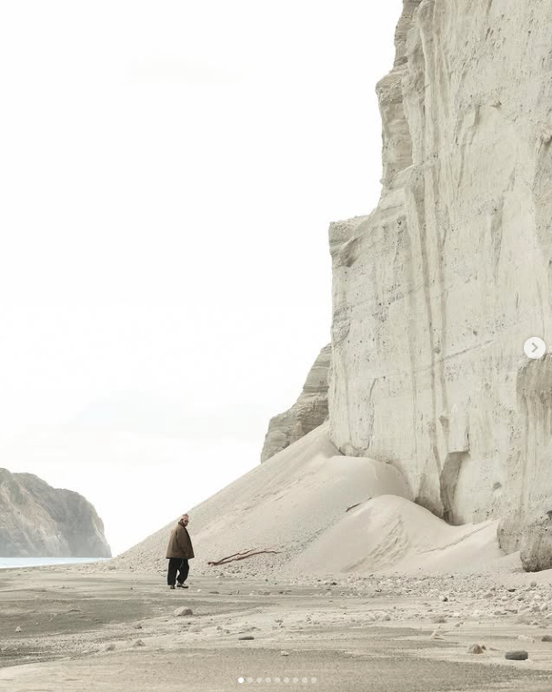 A solitary figure walking beneath a monumental pale coastal cliff
