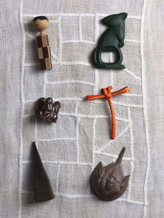 Small collected sculptural objects arranged on loose woven cloth