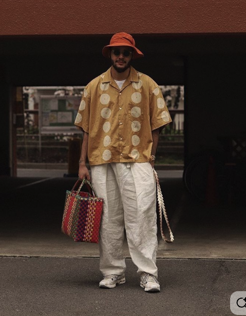 Front view of wide cream trousers styled with a mustard shirt and orange bucket hat