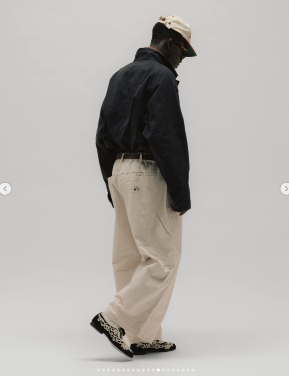 Rear three-quarter view of relaxed cream trousers shown mid-step